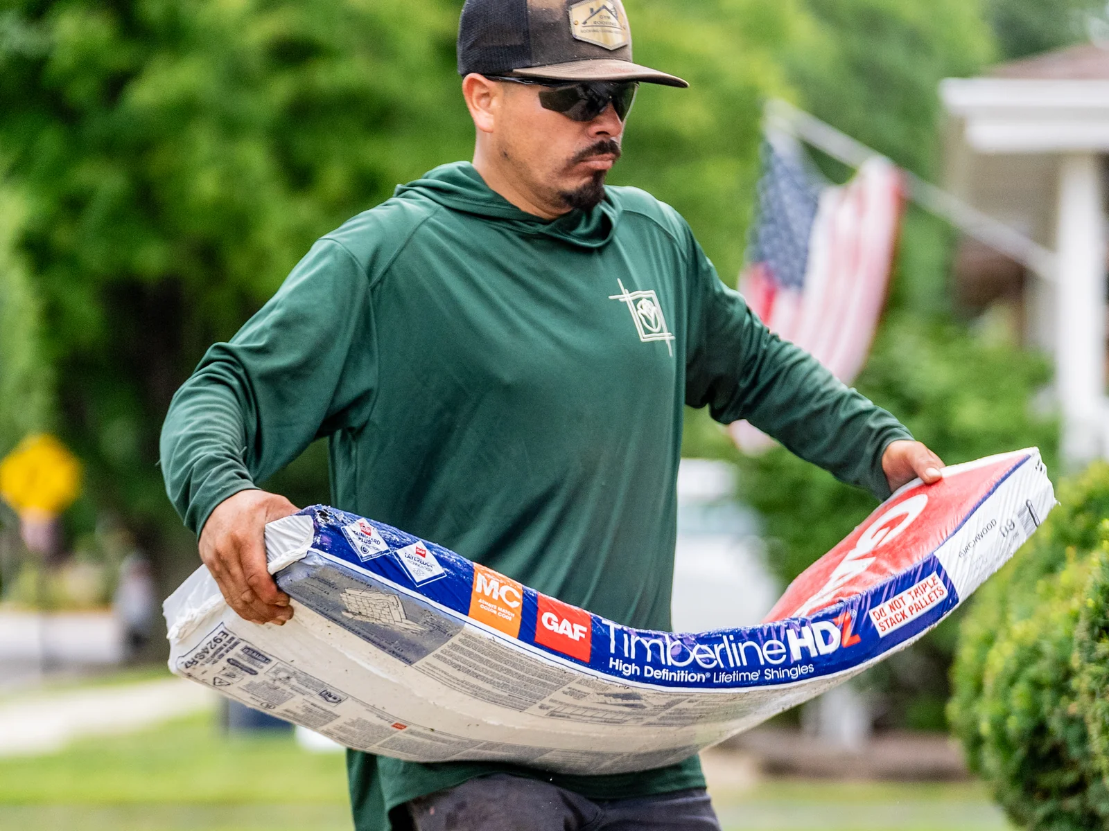 Rosales Roofing crew member carrying a GAF Timberline HDZ shingle bundle from the delivery pallet in Bolingbrook, Illinois