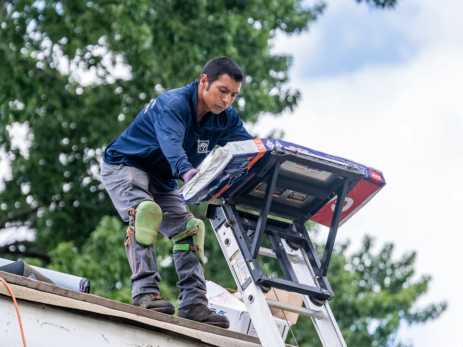 Rosales Roofing crew member taking a shingle bundle off the ladder hoist at the eave in Crestwood, Illinois
