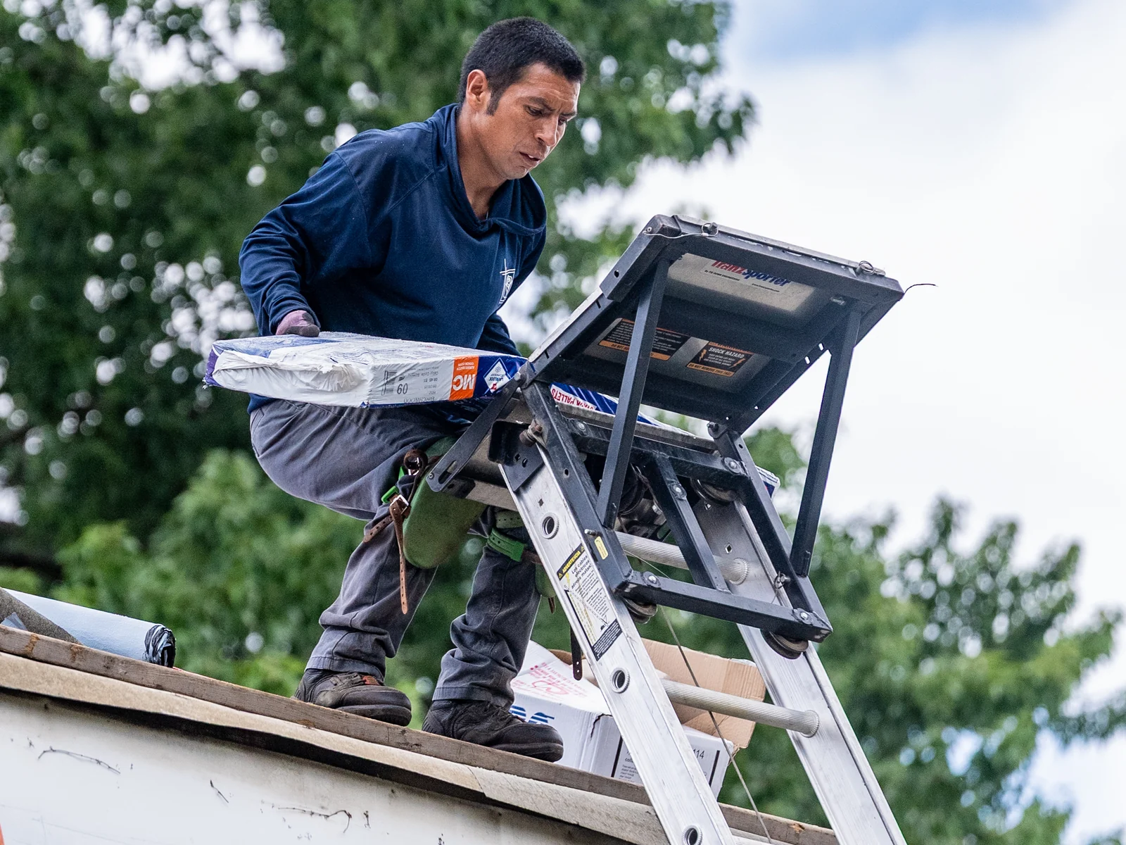 Rosales Roofing crew member unloading shingles from the ladder hoist at the roof edge in Monee, Illinois