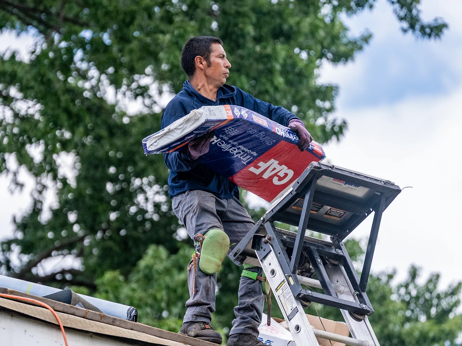 Rosales Roofing crew member lifting a GAF shingle bundle from the ladder hoist in Palos Park, Illinois