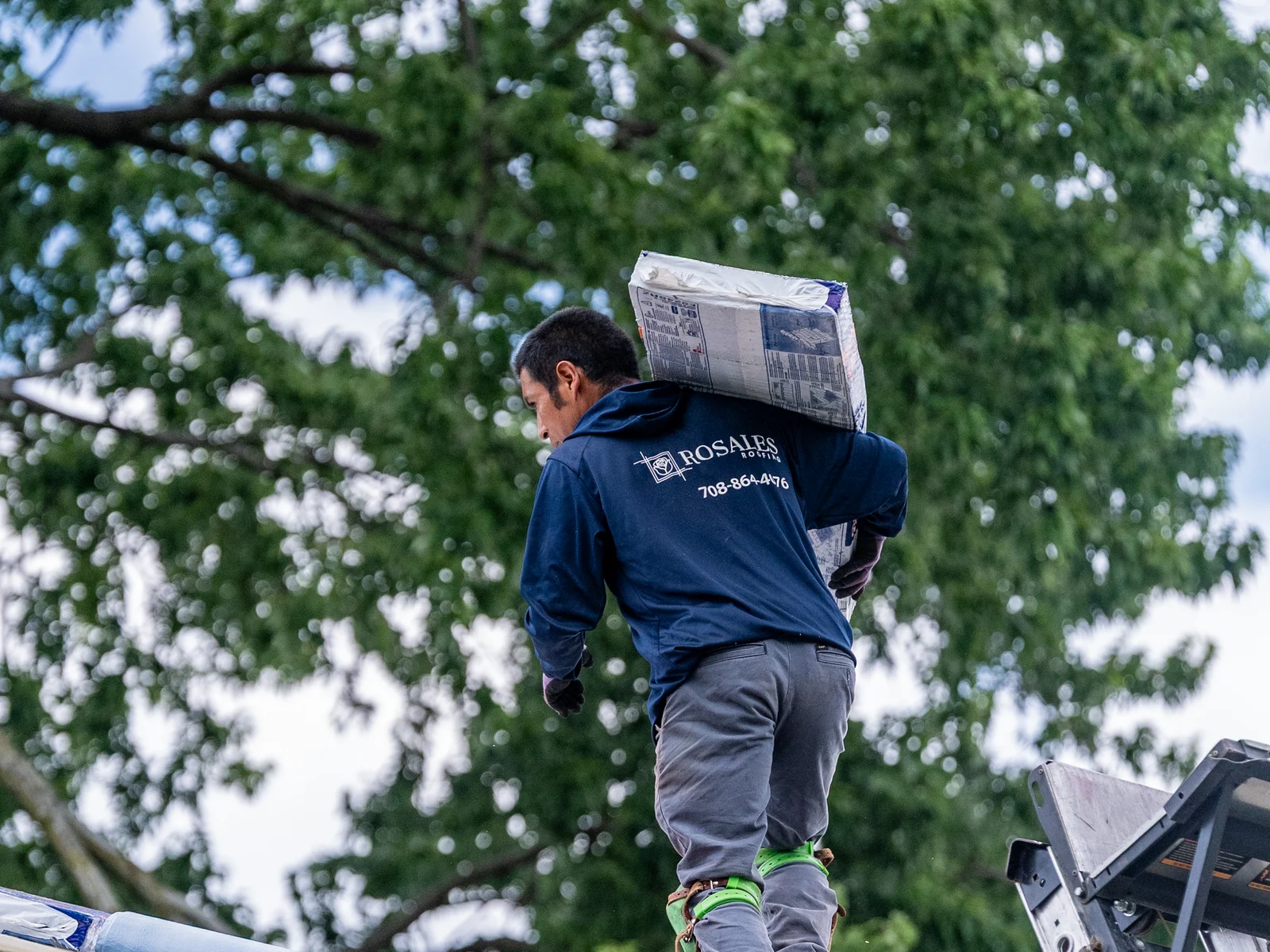 Rosales Roofing crew member carrying a shingle bundle across the roof in Palos Hills, Illinois