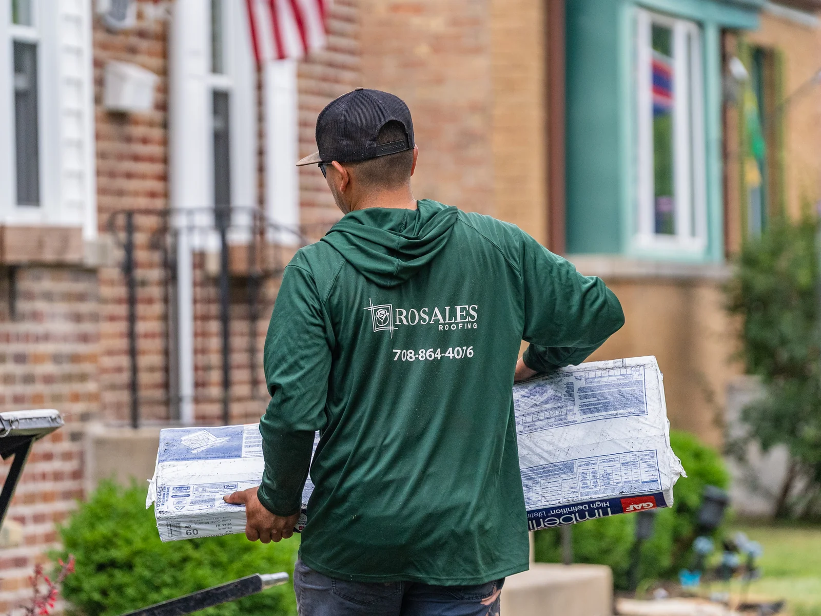 Rosales Roofing crew member carrying shingle bundles to the ladder hoist in Midlothian, Illinois