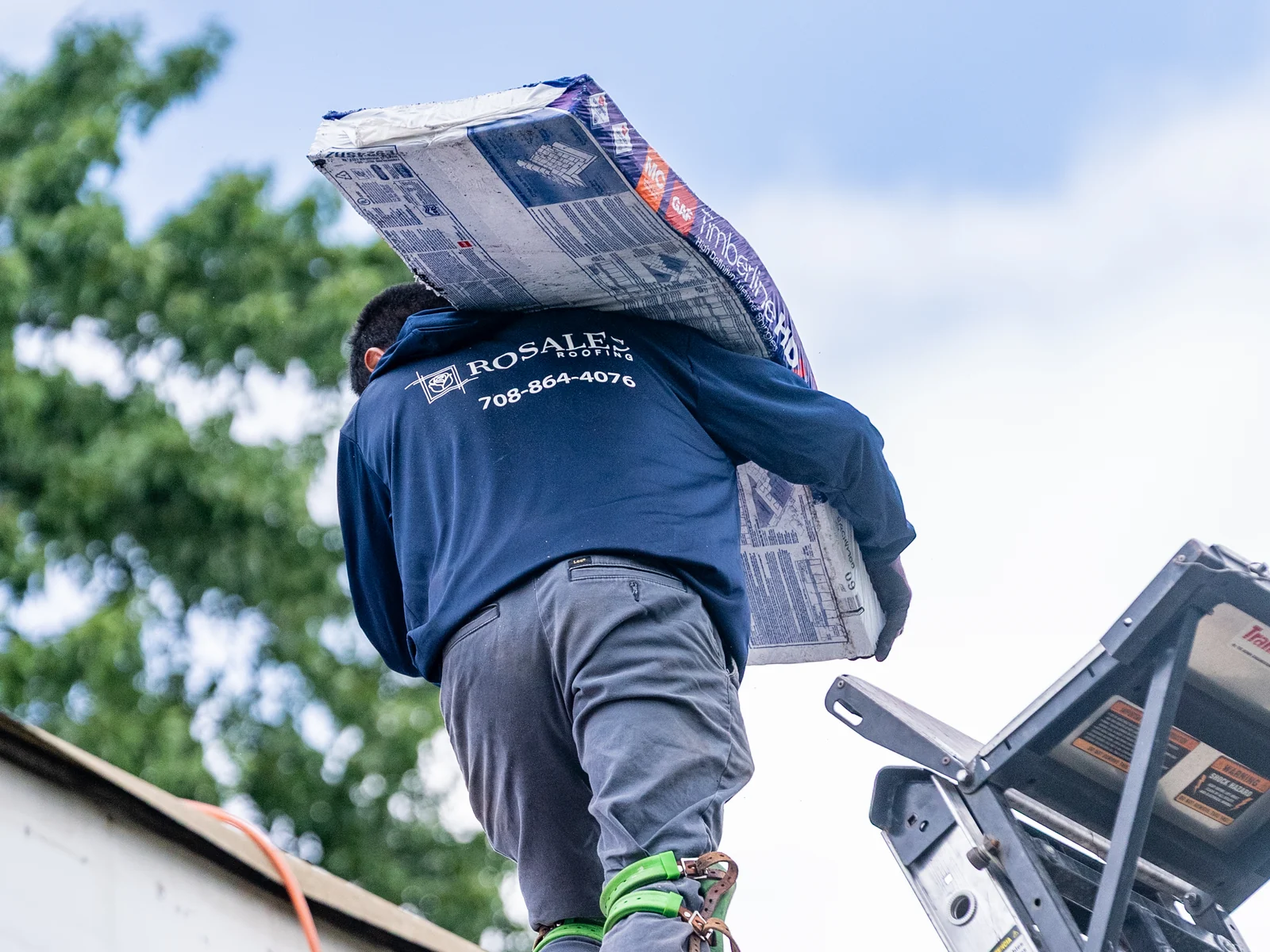 Rosales Roofing crew member carrying a shingle bundle up to the roof in Posen, Illinois
