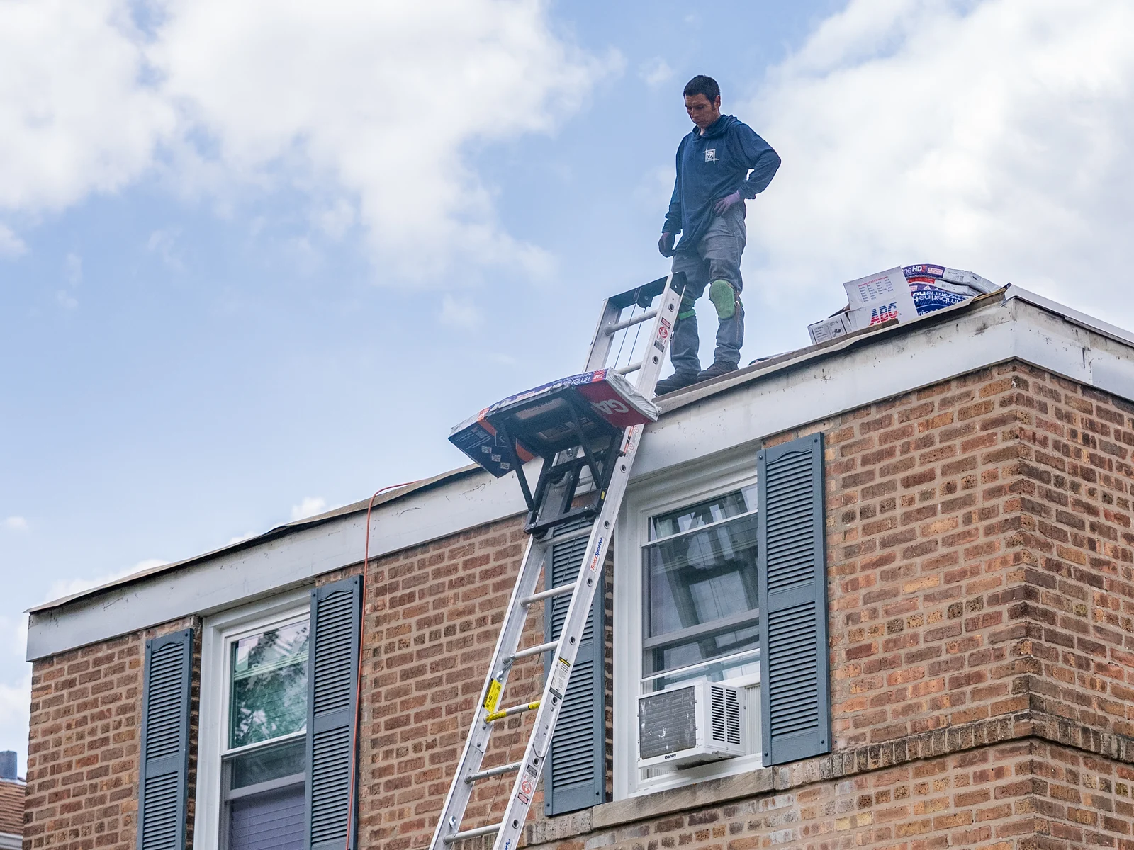 Rosales Roofing crew member at the roof edge with the ladder hoist raised to the eave in Harvey, Illinois